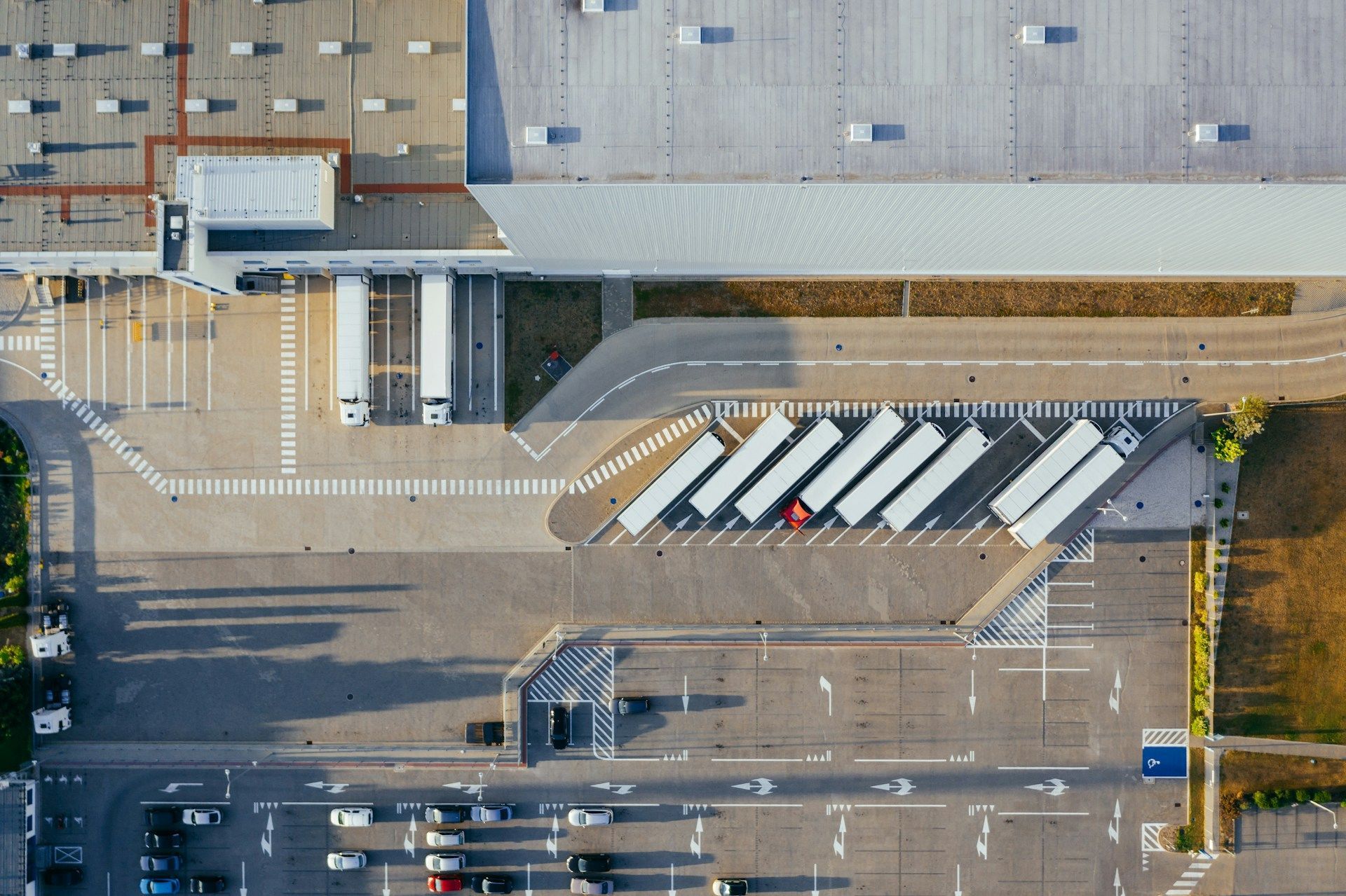 Aerial view of a bus terminal with parked coaches, road markings, and adjacent building entrances