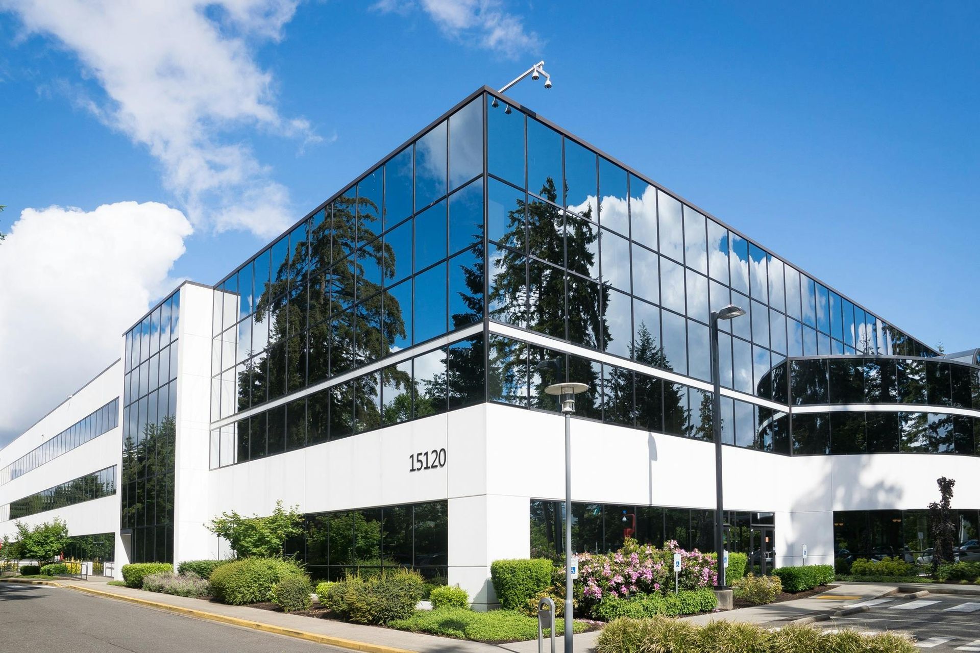 Modern glass office building with reflective blue windows and white facade beside a landscaped street