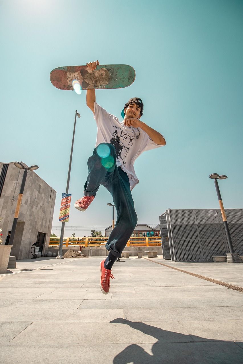 A skateboarder in mid-air, holding a board above his head. Bright blue sky background.