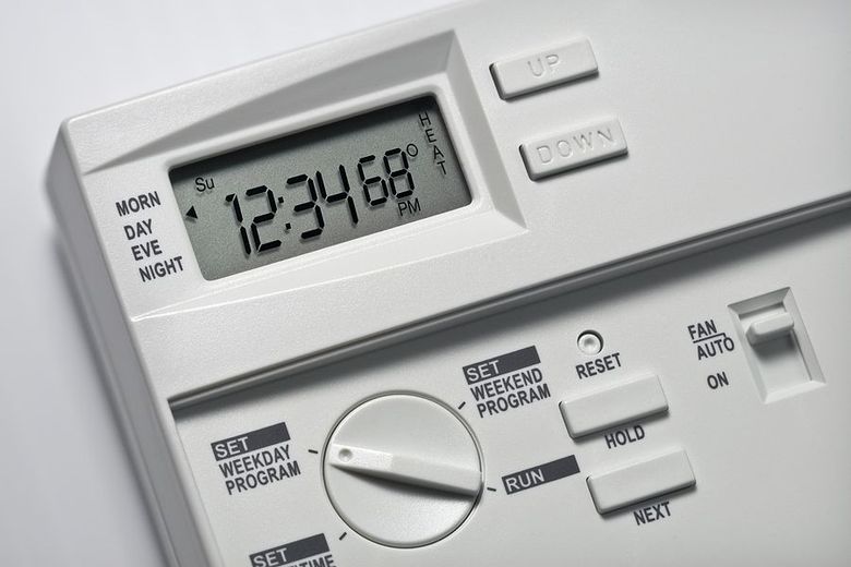 White thermostat displaying time, day, and set temperature, with buttons for adjustment and programming.