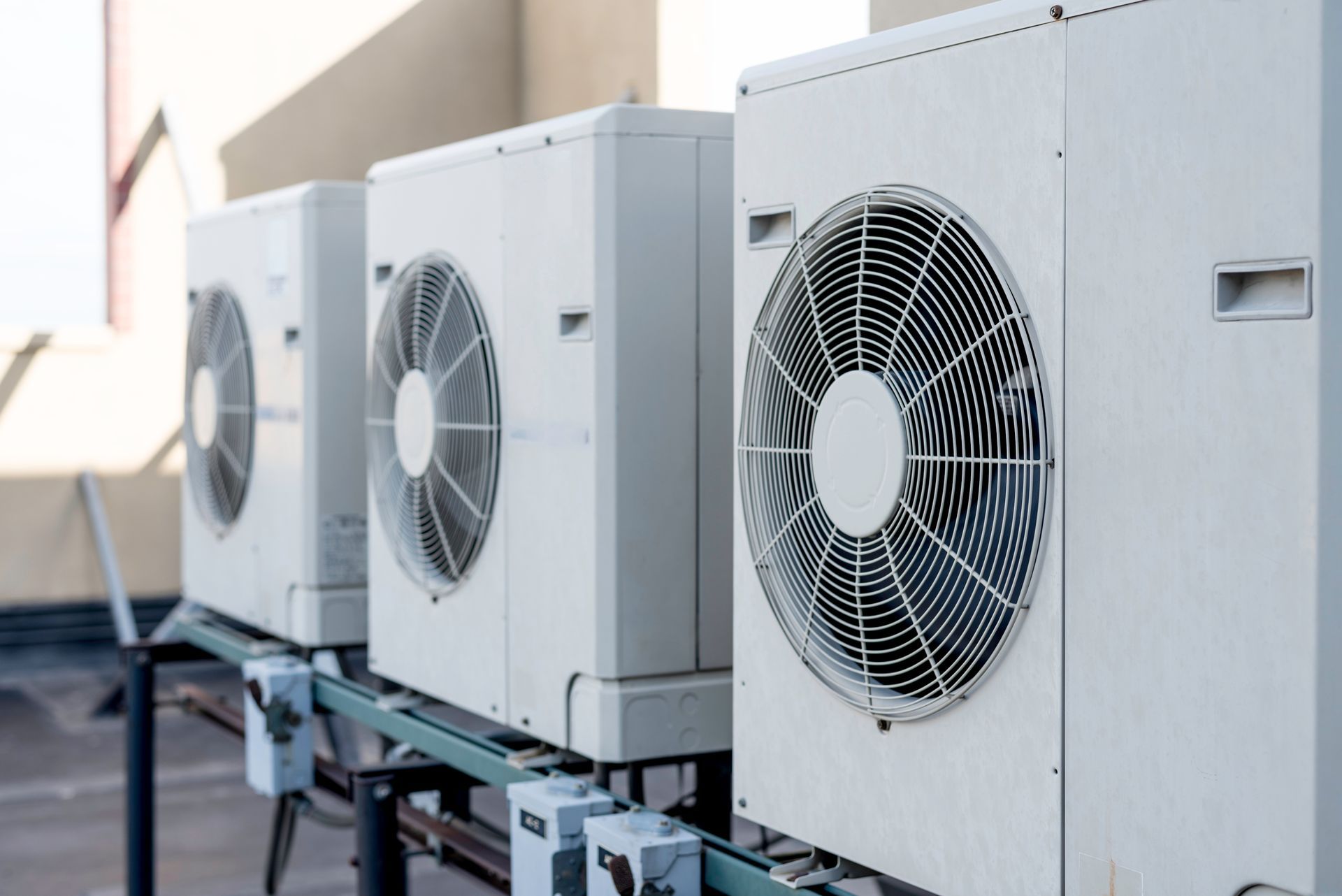Three white HVAC condenser units positioned in a row on a rooftop platform.