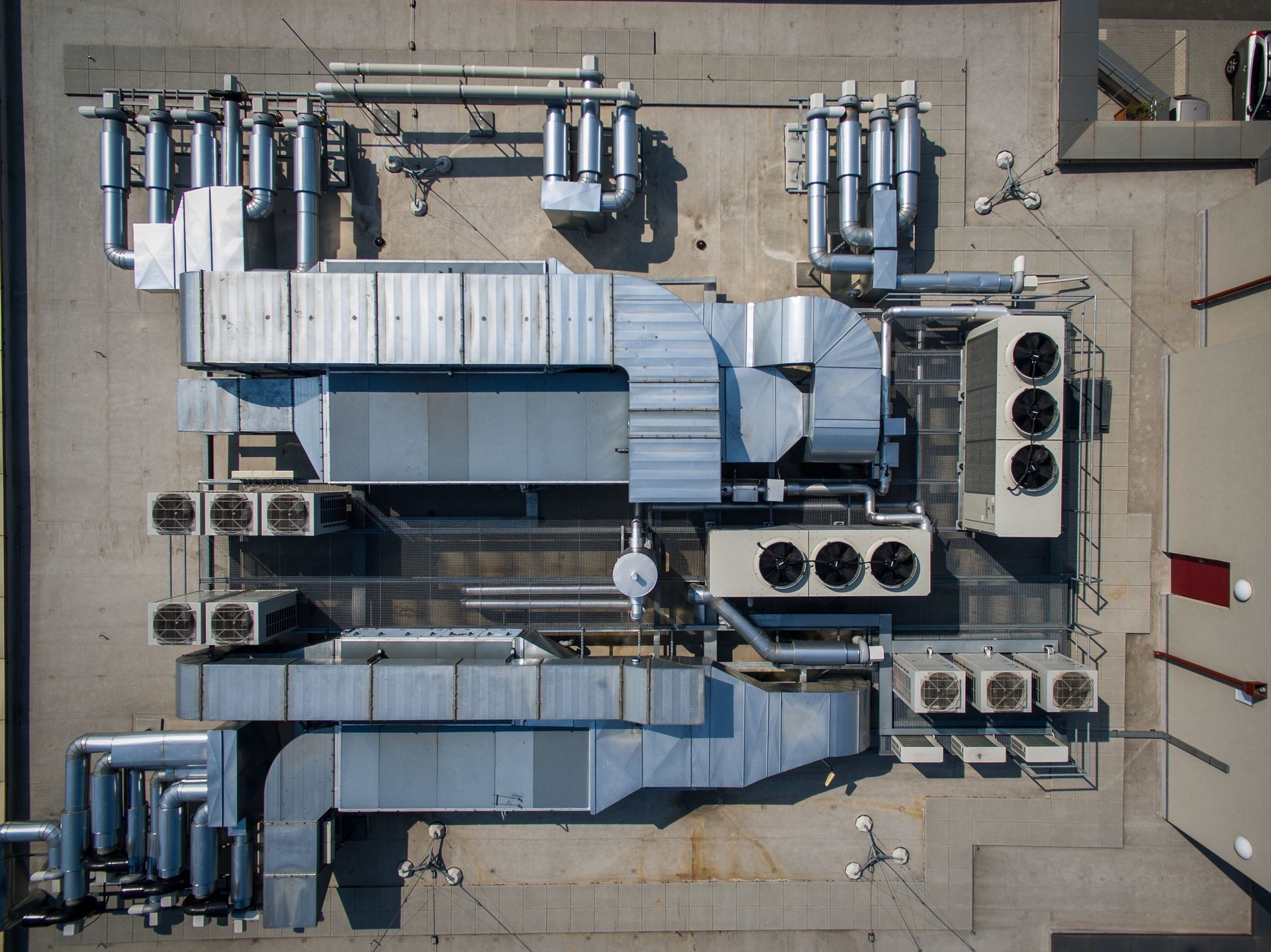 Top-down aerial view of a flat commercial roof featuring multiple silver HVAC units, ventilation ducts, and piping systems.