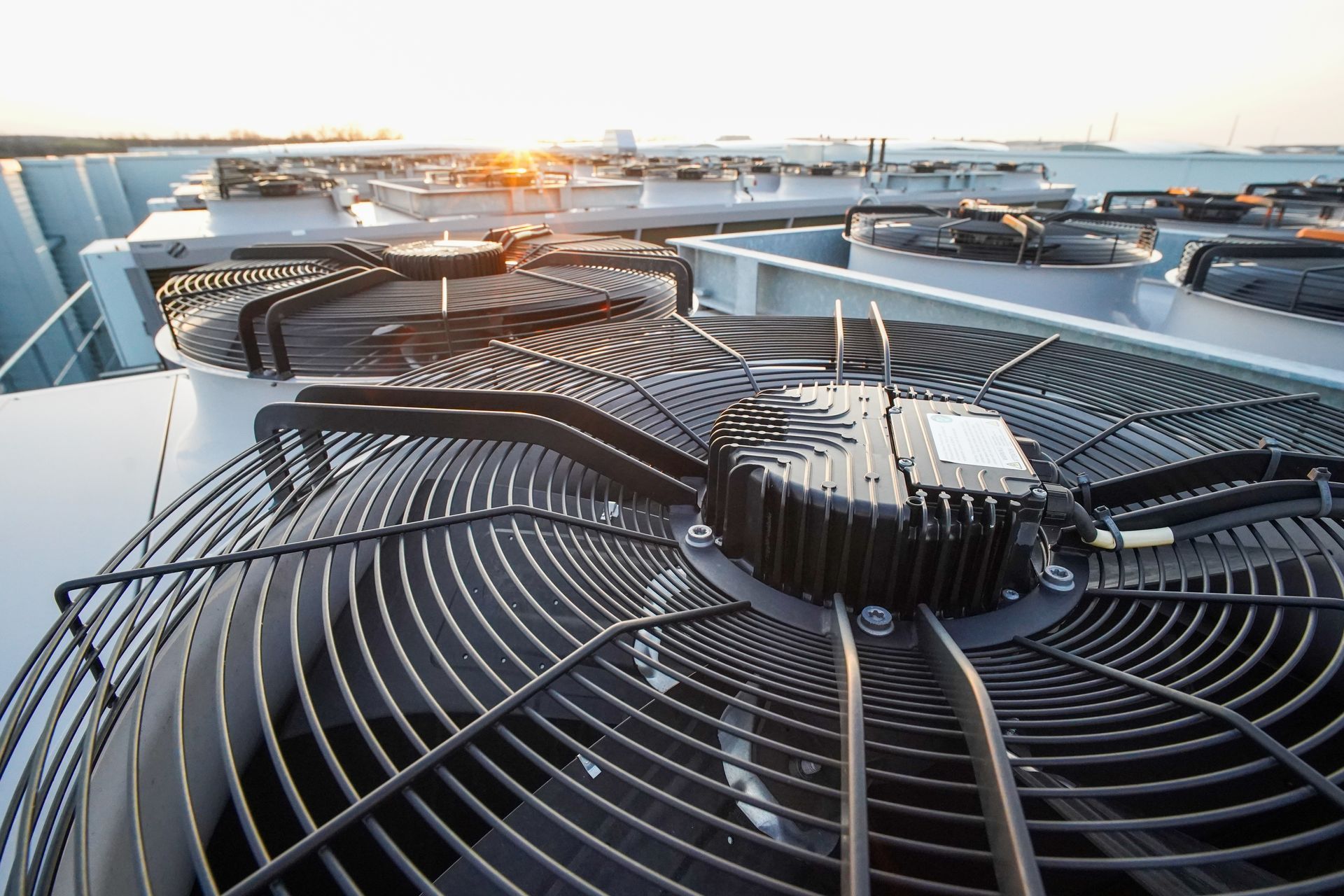 A close-up of large, black industrial cooling fans on a rooftop, with a sunset visible in the background.