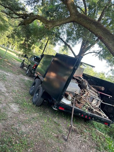 A dumpster trailer is parked on the side of a dirt road next to a tree.