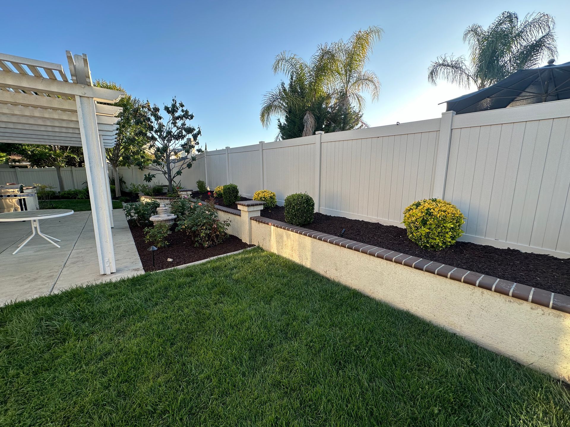 A backyard with a white fence and a pergola.