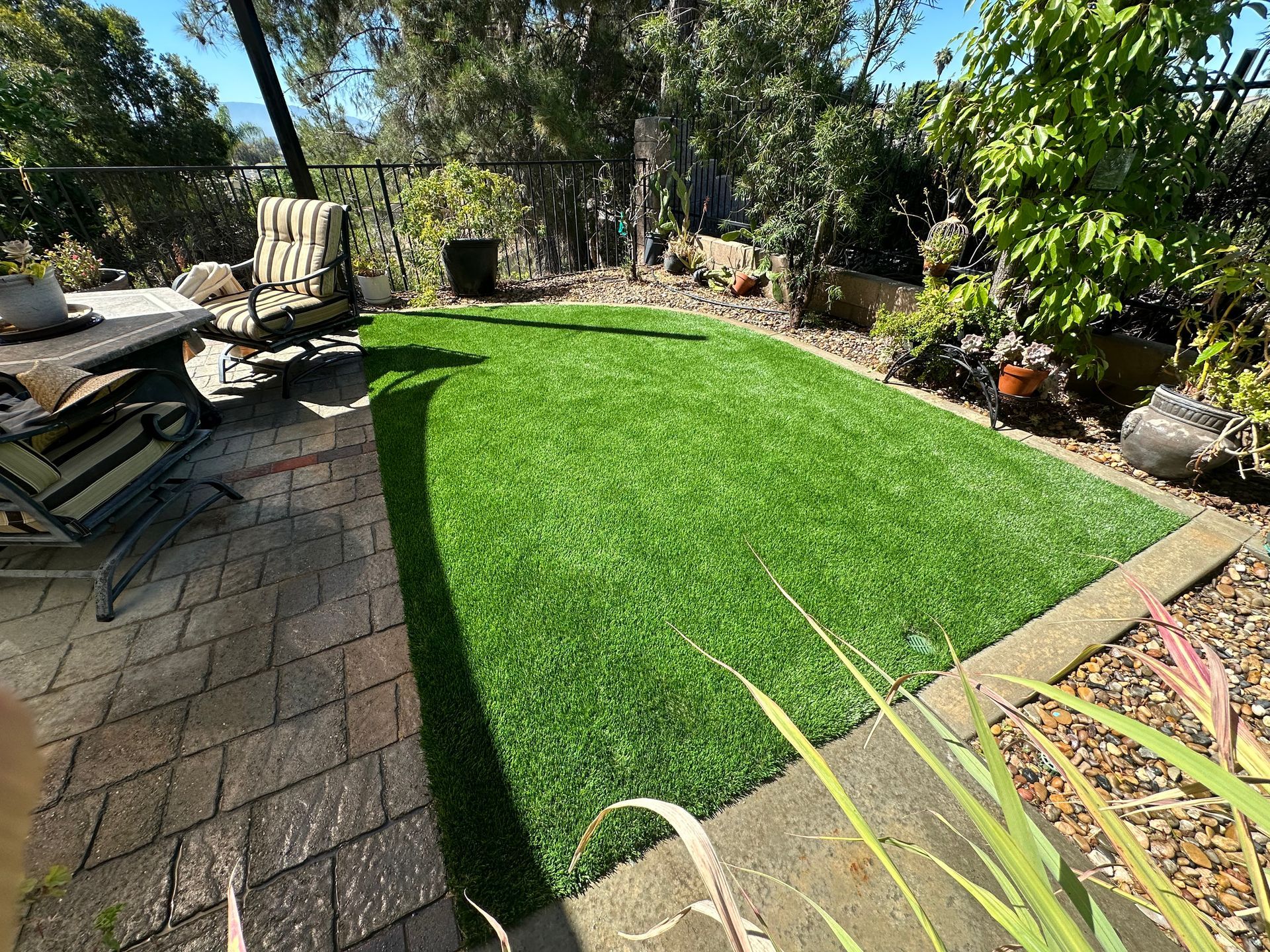 A lush green lawn with a patio and chairs in the background.