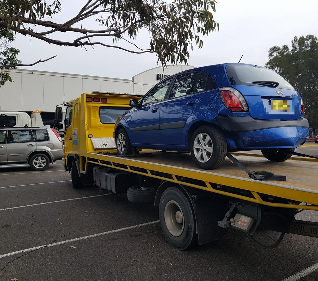 A Blue Car is Being Towed by a Yellow Tow Truck — Wyong and Tuggerah Towing Service in Wyee, NSW