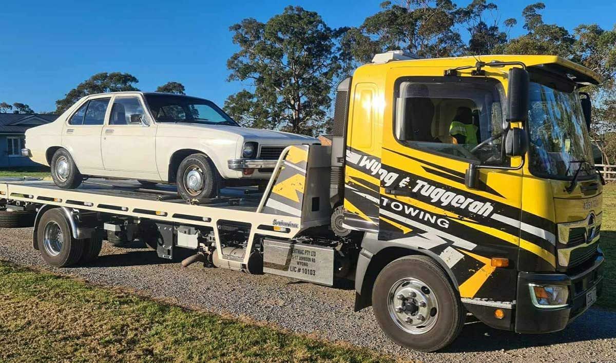 A Yellow Tow Truck is Carrying a White Car — Wyong and Tuggerah Towing Service in Tuggerah, NSW