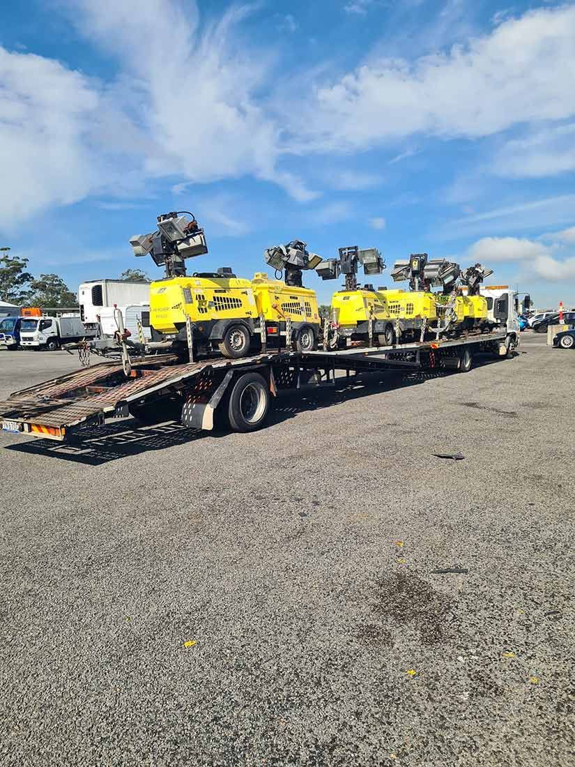 A Truck is Carrying a Bunch of Yellow Vehicles on a Trailer — Wyong and Tuggerah Towing Service in Tuggerah, NSW