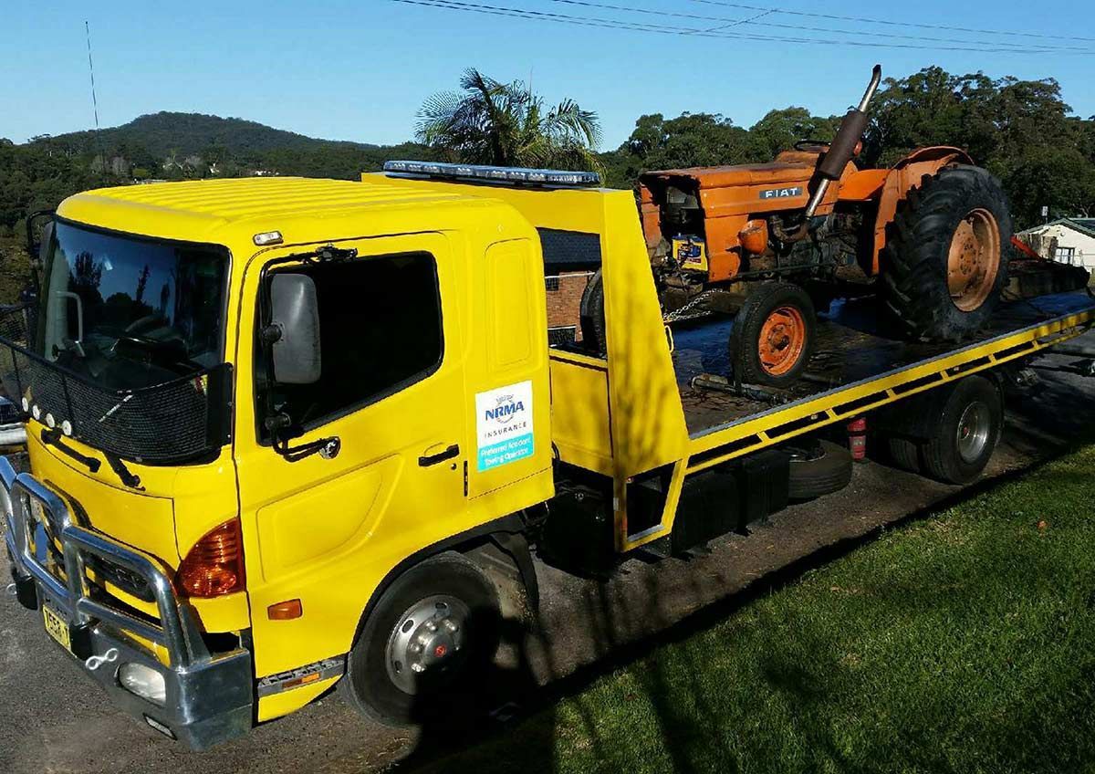 A Yellow Tow Truck With a Tractor on the Back of It — Wyong and Tuggerah Towing Service in Tuggerah, NSW