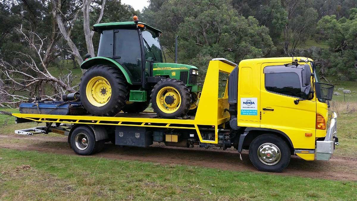 A Yellow Tow Truck is Carrying a Green Tractor — Wyong and Tuggerah Towing Service in Budgewoi, NSW