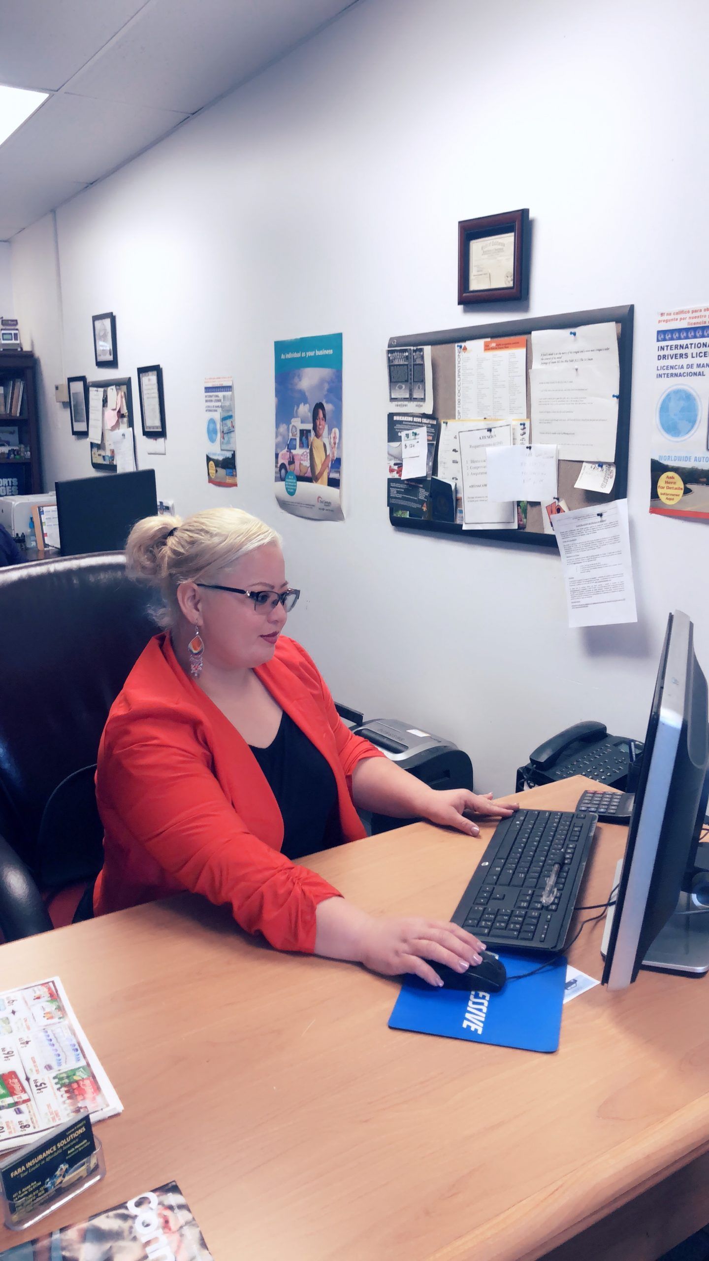A woman in a red jacket is sitting at a desk using a computer.