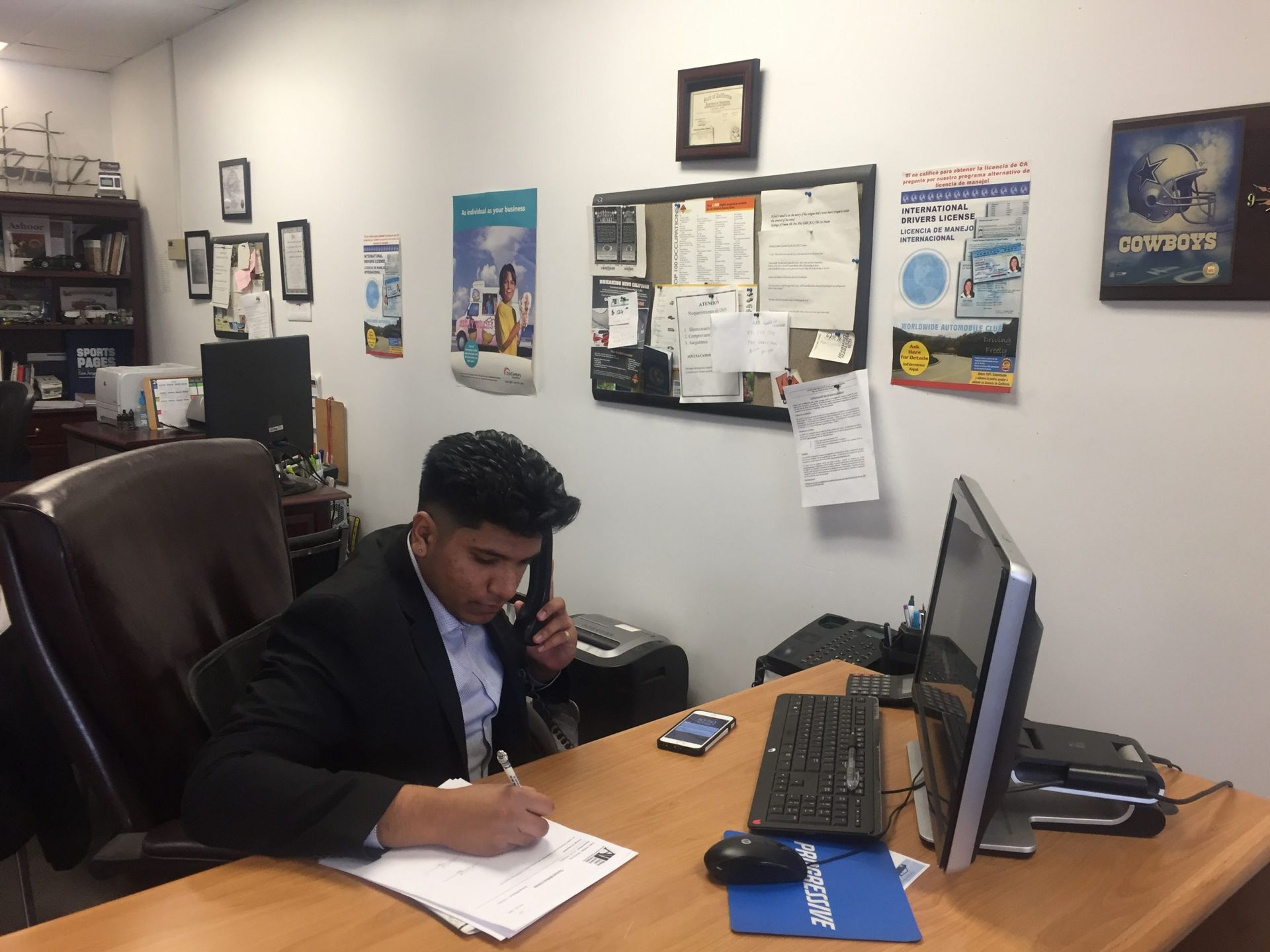 A man is sitting at a desk talking on a cell phone