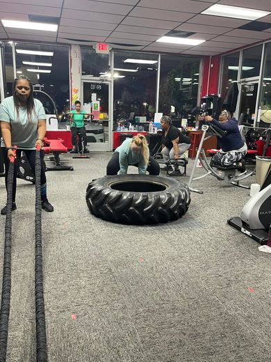 People working out in a gym. One uses battle ropes; another flips a tire. Others use various equipment.