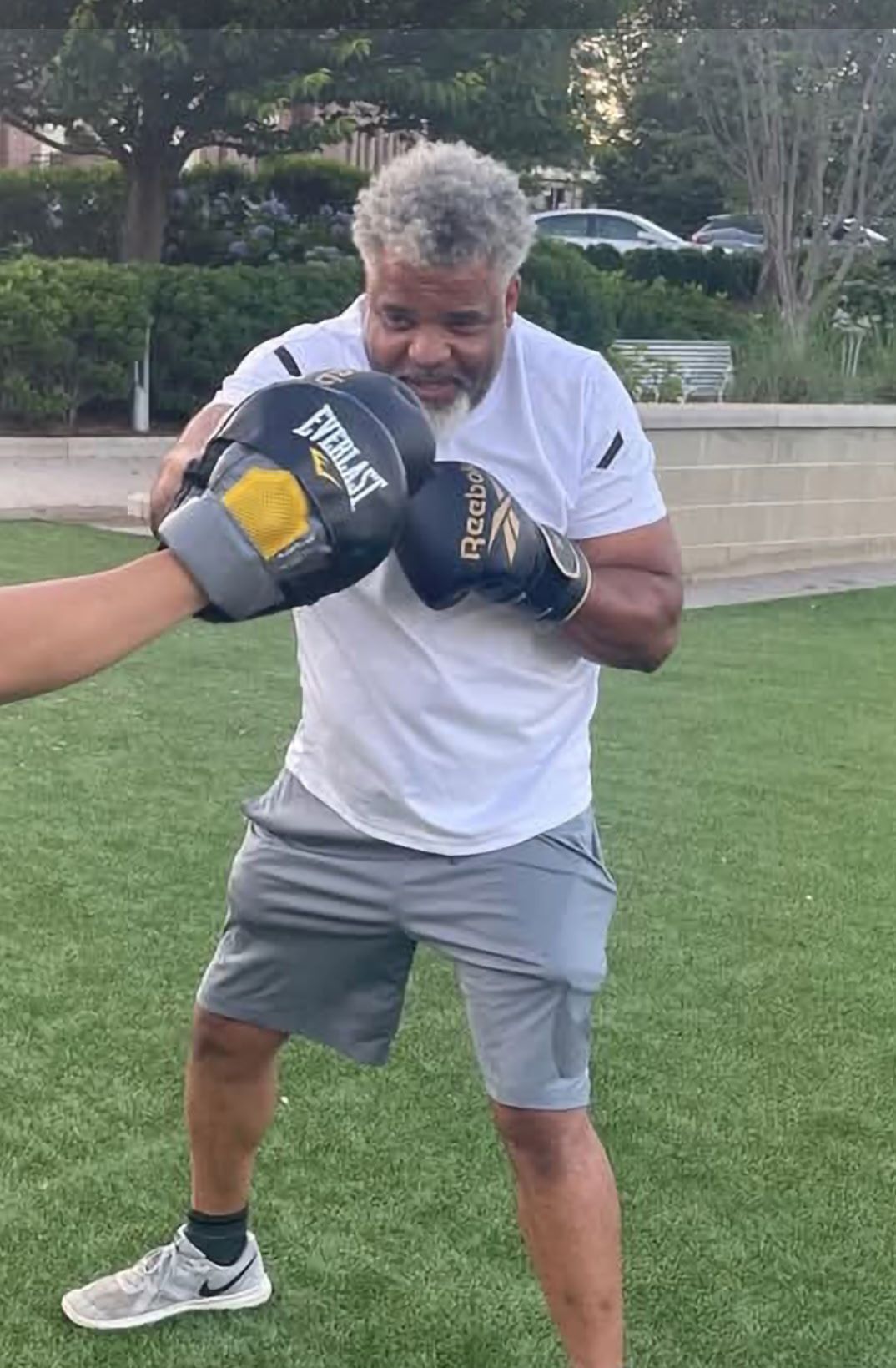 Man in boxing stance, wearing gloves, in a park.