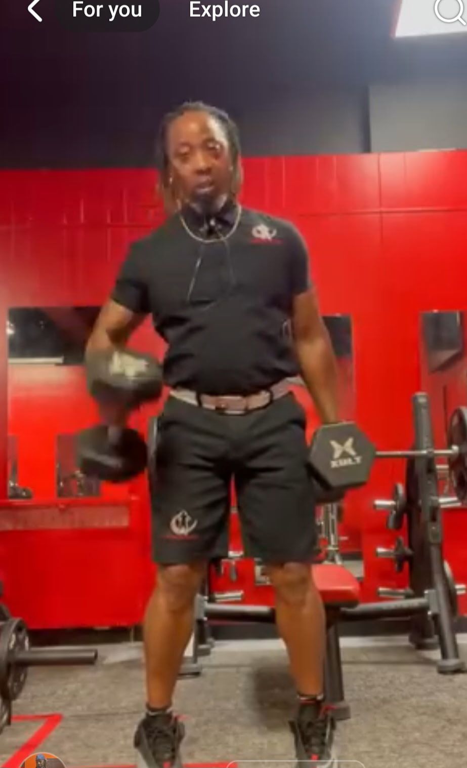 Man in black gym attire working out with dumbbells in a red gym.