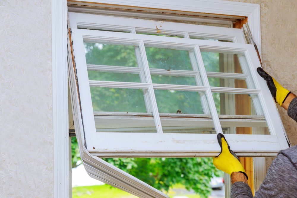 Hands Wearing Yellow Gloves Removing a White Window From a Frame — Sams Glass Solutions in Bowen, QLD