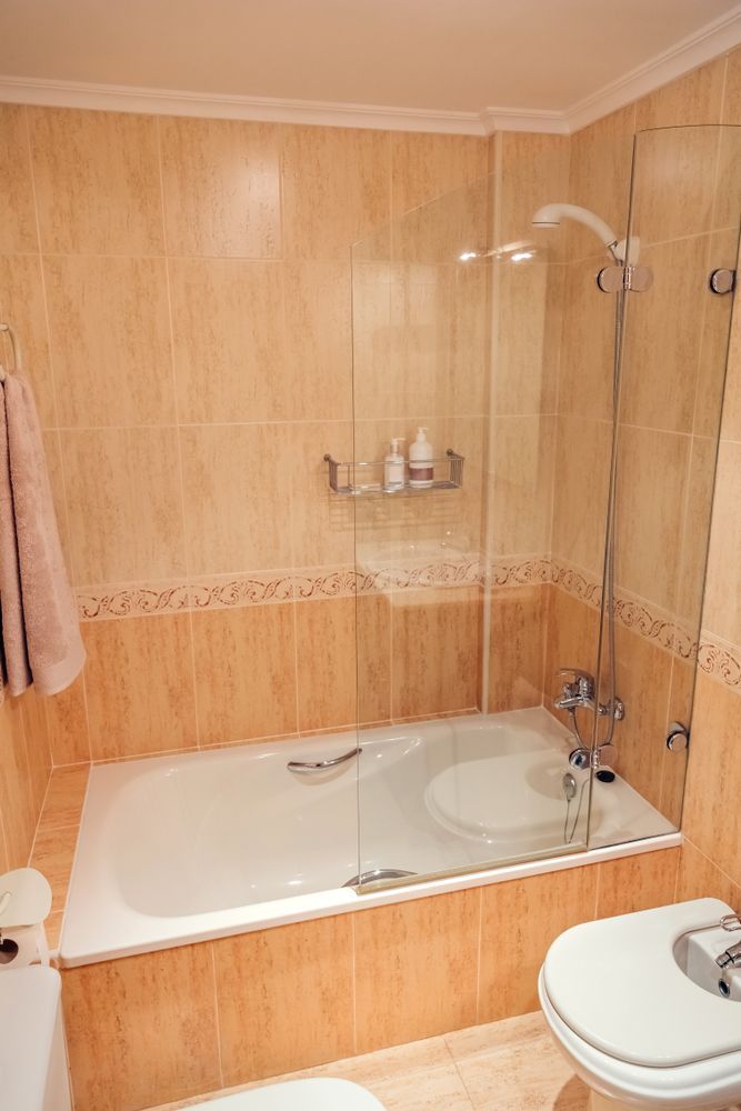 Bathroom With a Beige Tiled Wall and a Bathtub With a Clear Glass Shower Door — Sams Glass Solutions in Bowen, QLD