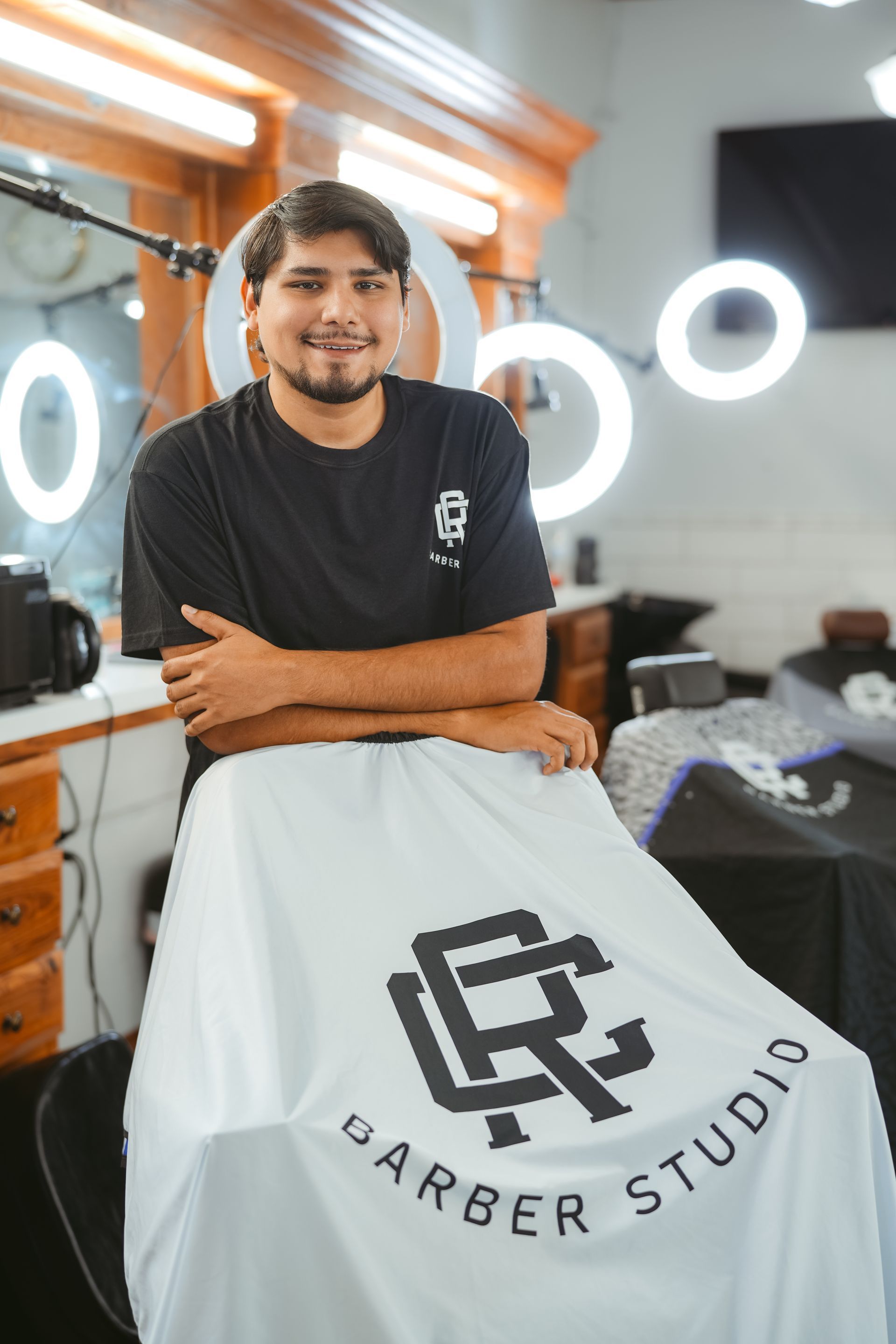 Barber standing behind a white barber cape with a logo that says 