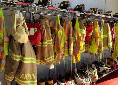 A row Akron firefighters' uniforms and helmets hanging on a rack.