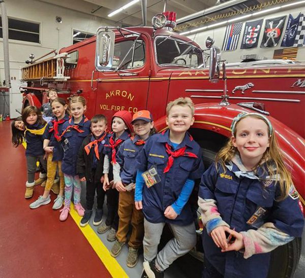 Children from Scouts troop standing in front of older fire engine.
