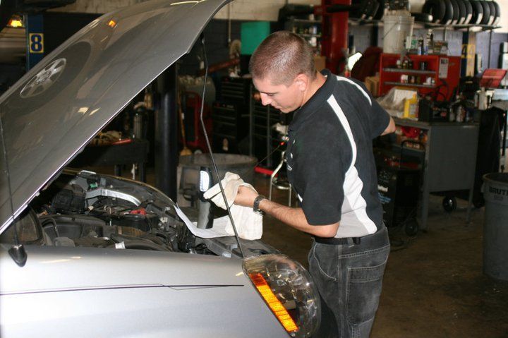 A mechanic in a black uniform cleans under the hood of a car inside a repair shop. | Ocello’s Automotive Center