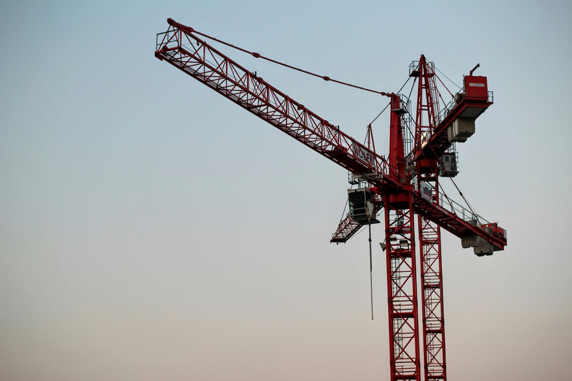 Red construction crane against a light blue and peach sky.