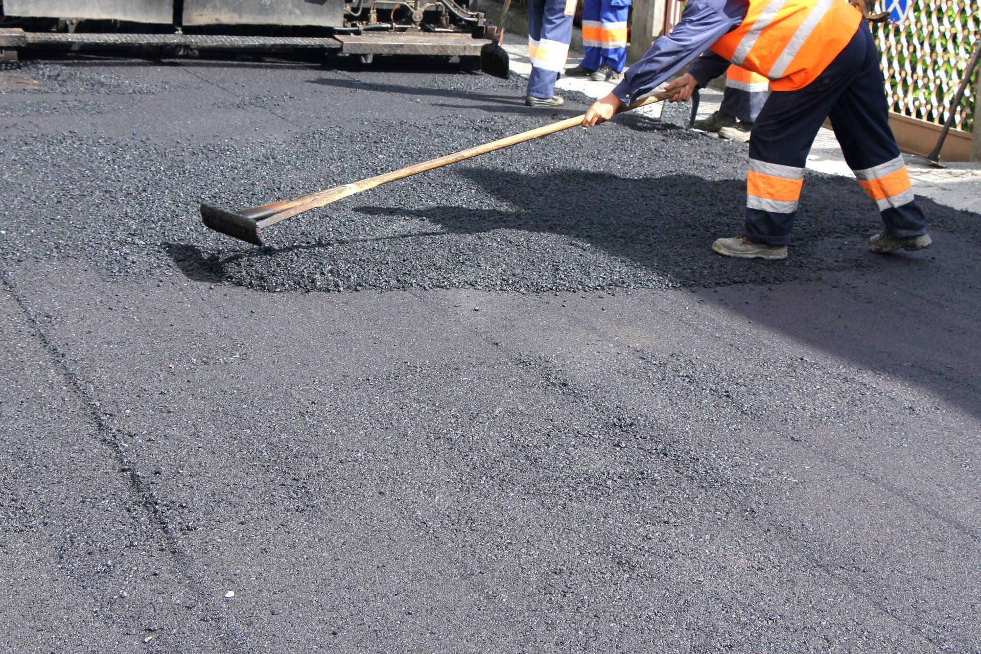 A man is spreading asphalt on the ground with a rake.