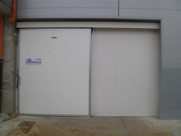 Porta scorrevole bianca isolata su un edificio industriale grigio.