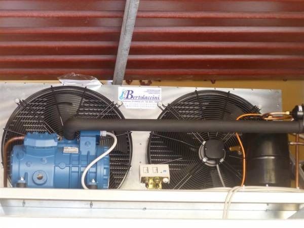Unità di refrigerazione blu con due ventole, montata all'esterno sotto un tetto in lamiera ondulata rossa.