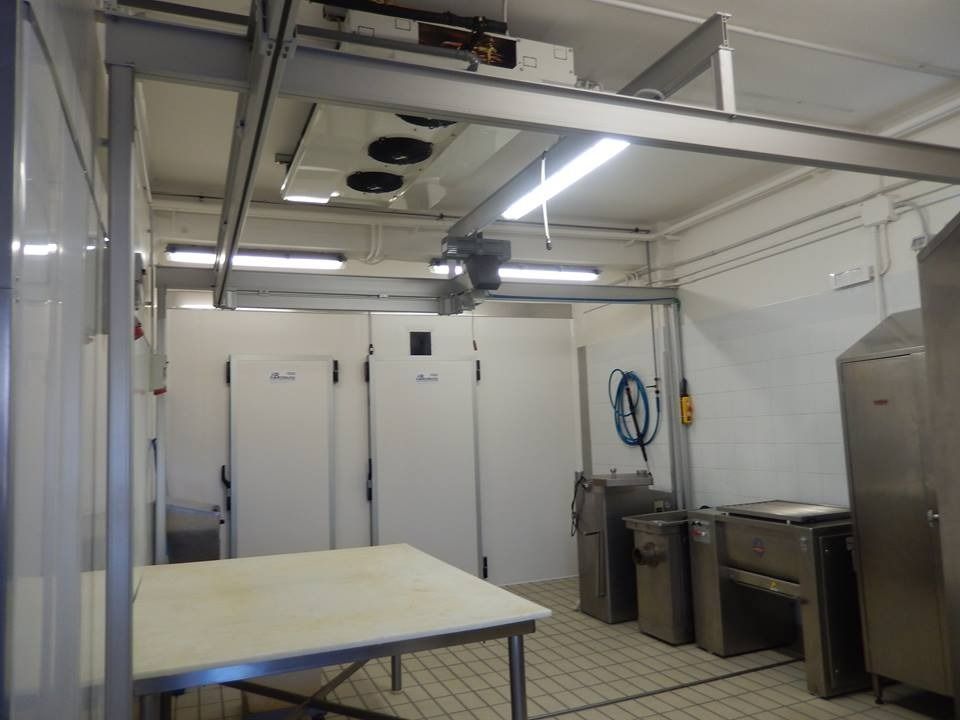 Sala di lavorazione della carne con pareti bianche, frigoriferi e sistema di binari sopraelevati.