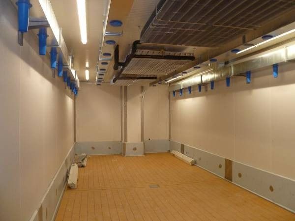 Stanza rettangolare vuota con pareti bianche, pavimento effetto legno e lampadari a soffitto.