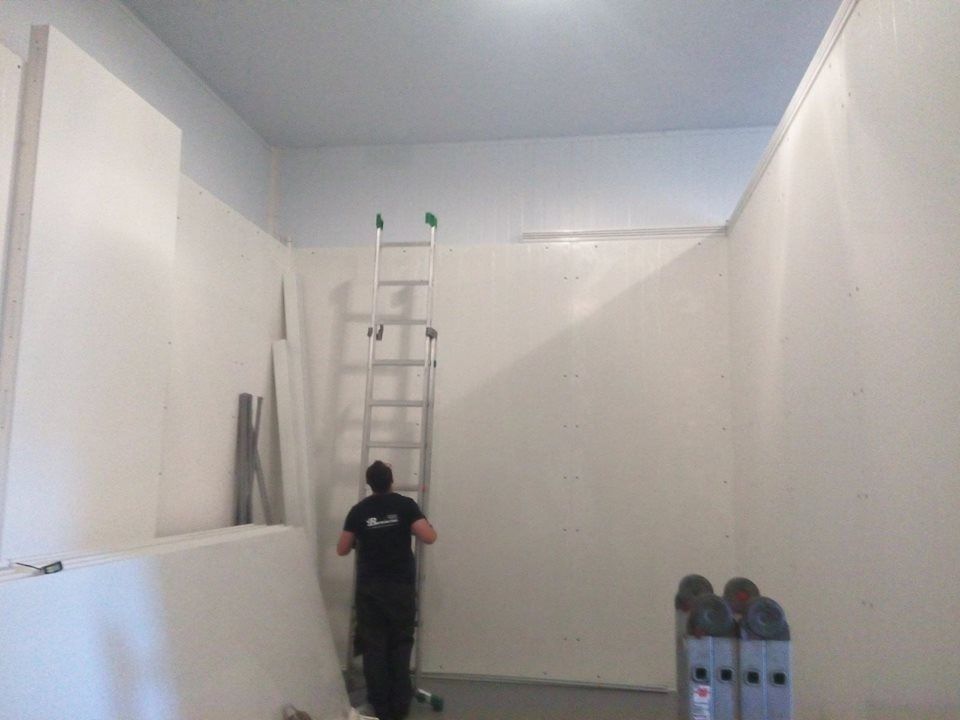 Persona su una scala che dipinge il soffitto di una stanza con pareti bianche e una sezione del soffitto blu.