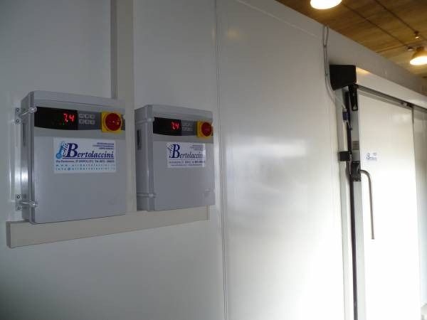 Due pannelli di controllo su una parete bianca, vicino a una porta scorrevole; interno di un'unità di refrigerazione.