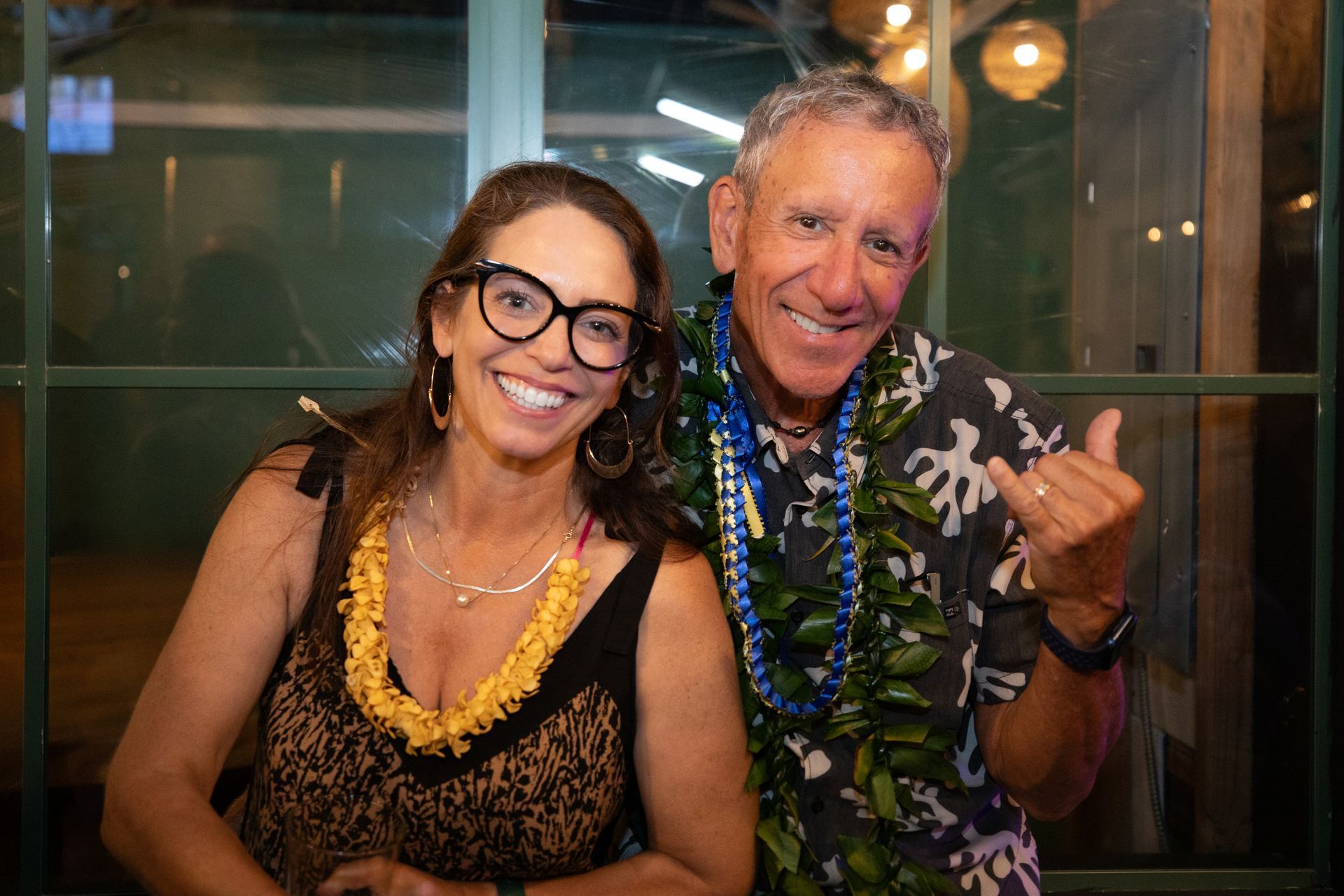 A man and a woman are posing for a picture . the man is wearing a lei and the woman is wearing glasses.