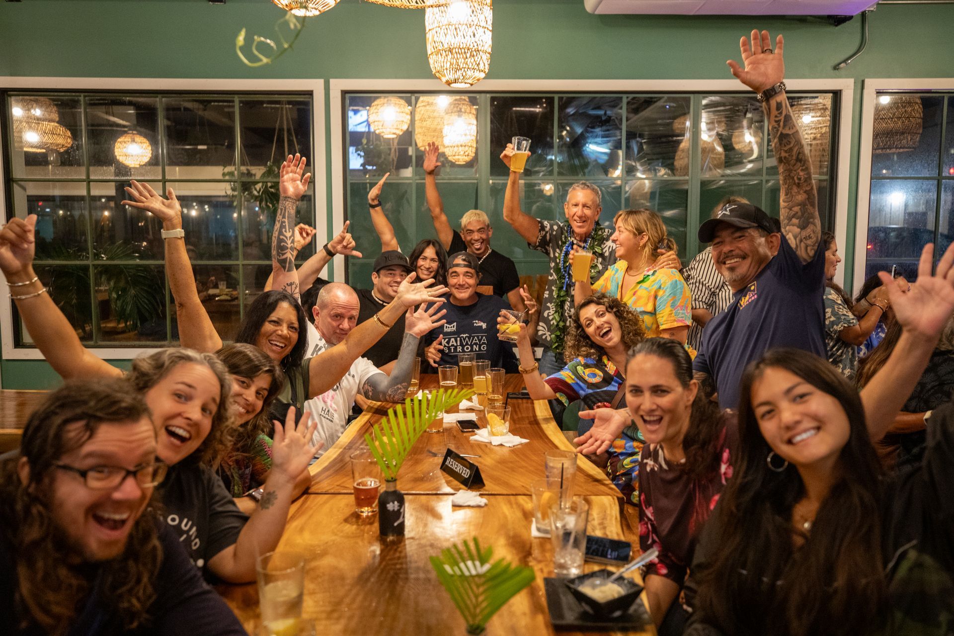 A group of people are sitting at a table with their arms in the air.