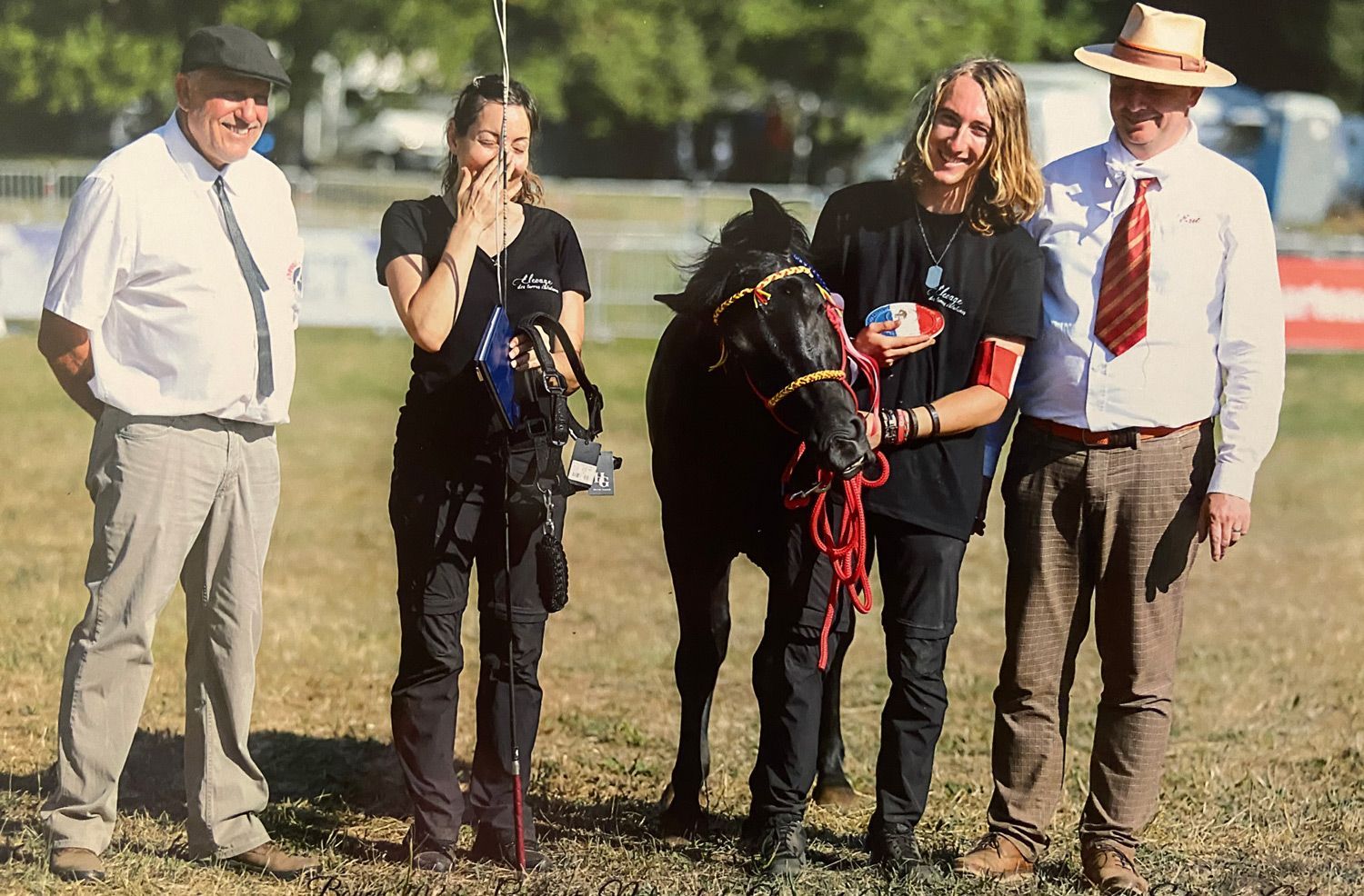Des personnes accompagnent un poney noir lors d'un événement en plein air. Deux personnes tiennent le poney. D'autres les observent.
