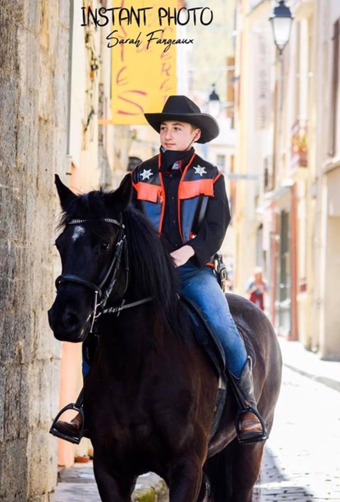 Une personne à cheval, vêtue en cow-boy, traverse une rue étroite et ensoleillée.
