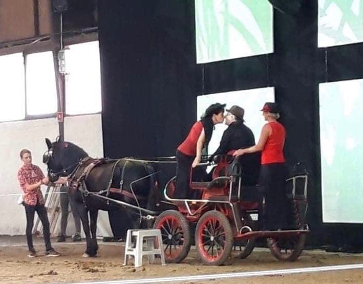 Calèche avec des personnes qui s'embrassent. Une personne se tient debout sur la calèche, les autres autour. Décor d'intérieur, évoquant une scène.