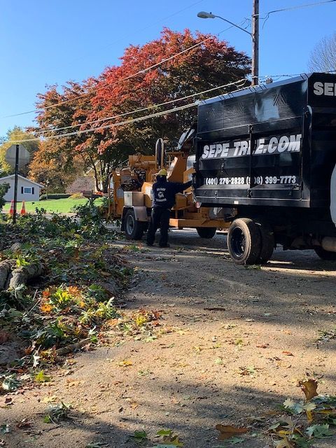 A man is standing next to a tree chipper truck.