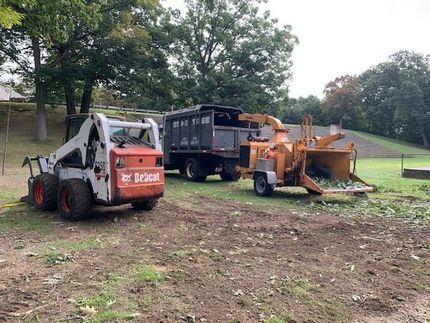 A bobcat skid steer and a wood chipper are parked in a dirt field.