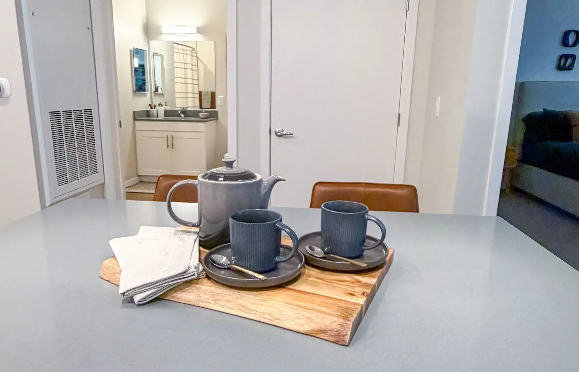 Dining table with a teapot and two mugs on a wooden tray in an apartment kitchen.
