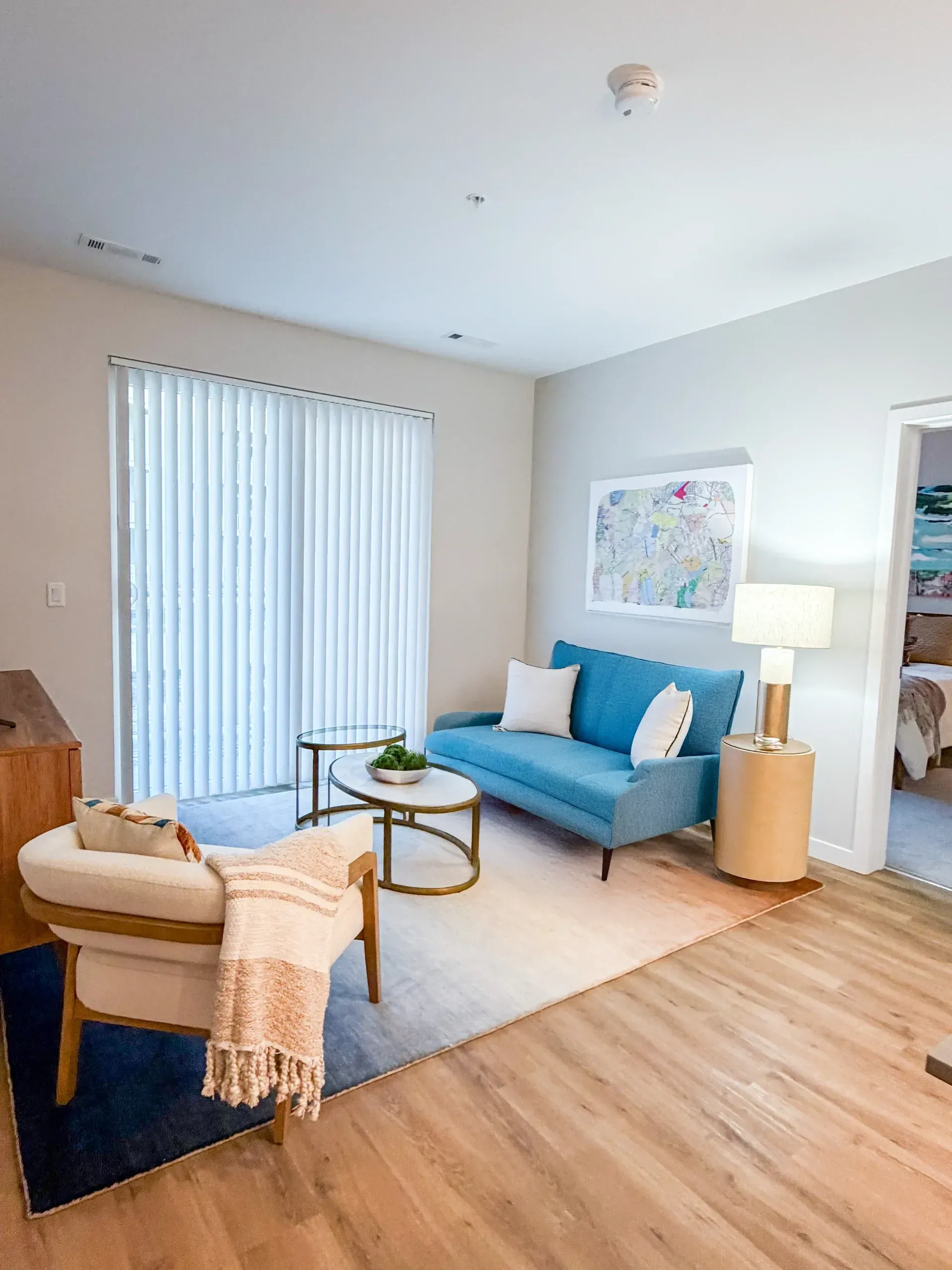 Living room in an apartment with a blue sofa, white chair, coffee tables, lamp, and wall map.