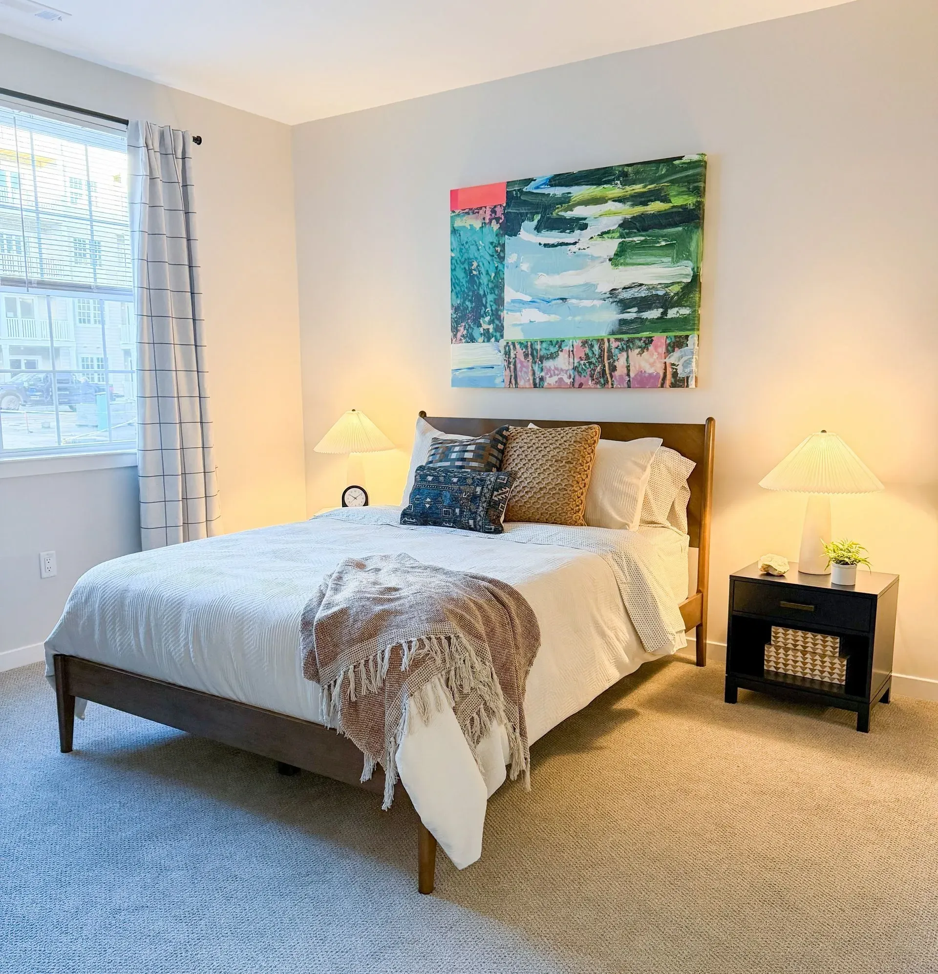 Bedroom with a wooden bed, two nightstands, lamps, and an abstract painting on the wall.