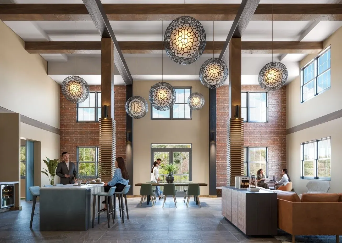 Open residential lobby with brick walls, large windows, and round pendant lights; several residents sit and chat.