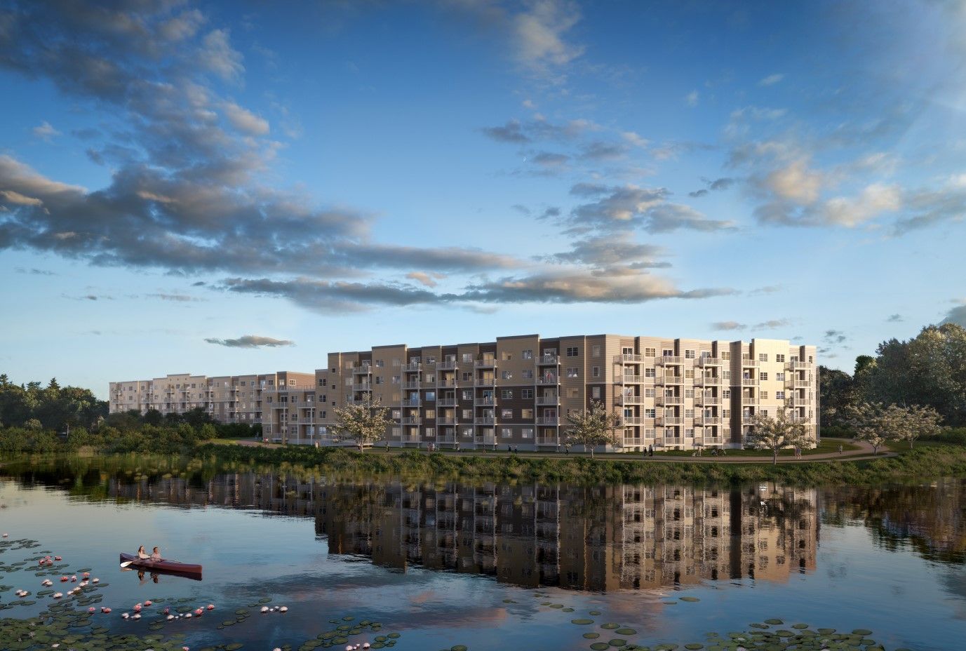 Exterior view of a modern apartment complex beside a lake with trees and a blue sky.