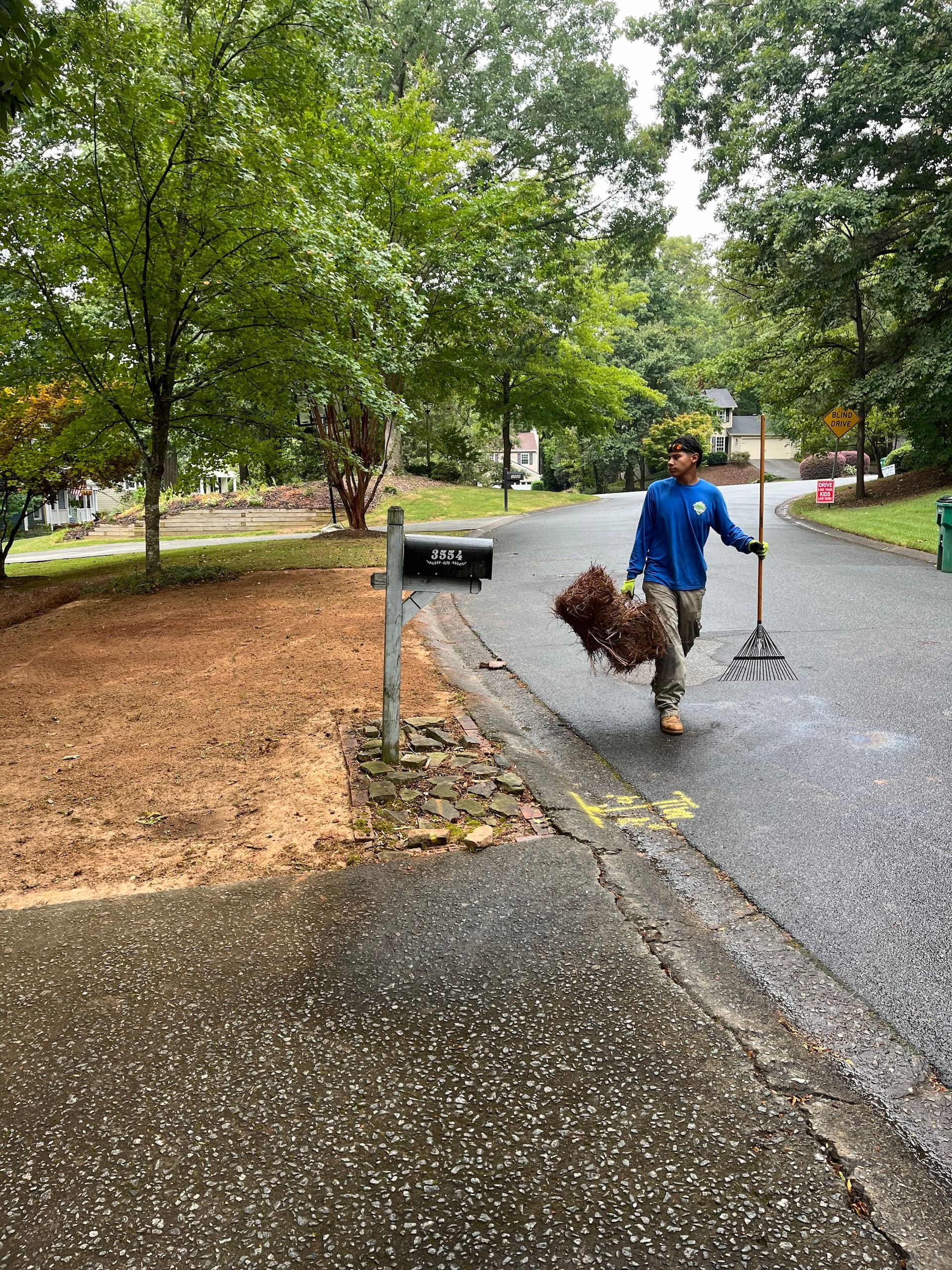 A man is walking down a street with a rake in his hand.