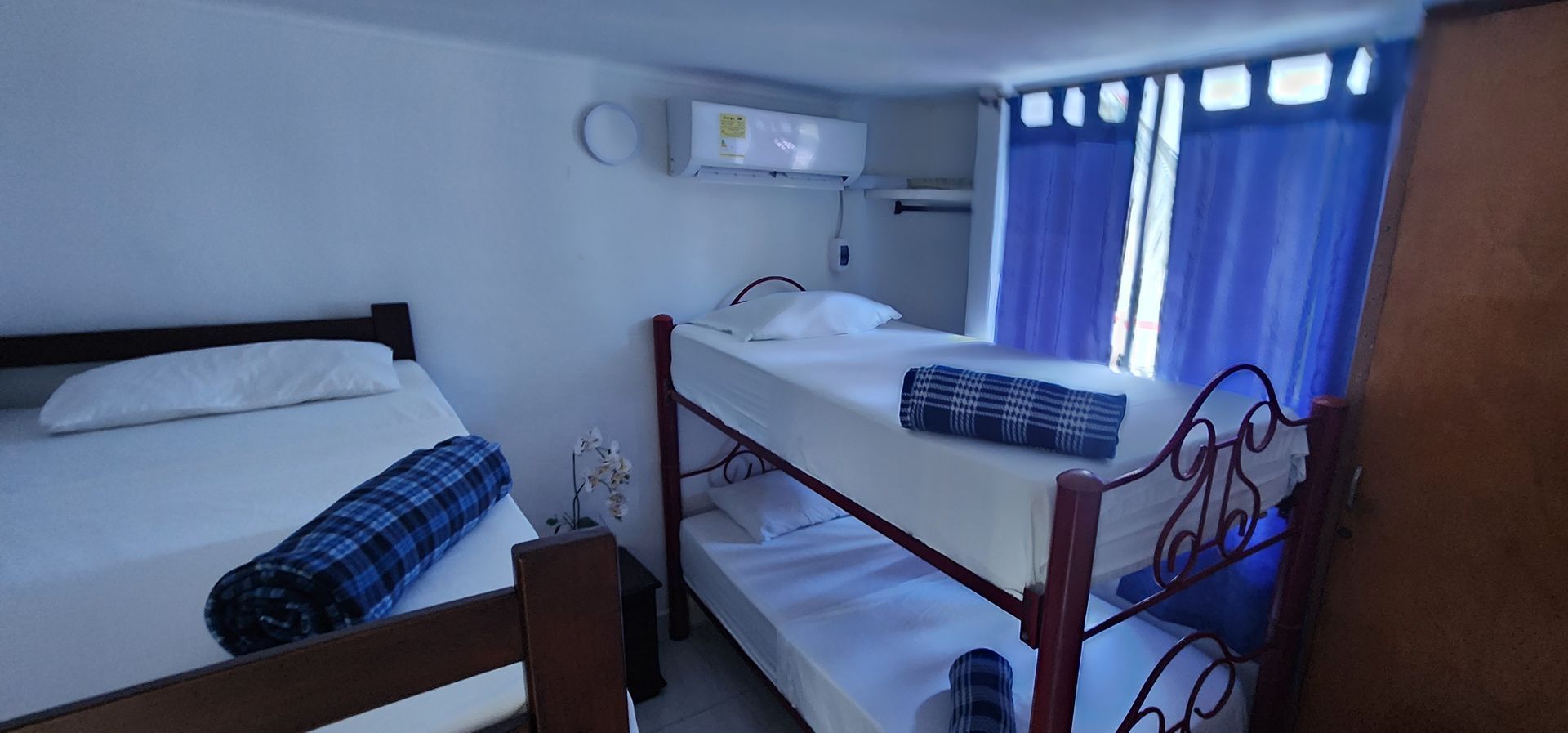 Un dormitorio con una cama doble a la izquierda y una litera a la derecha, ambas con sábanas blancas y mantas estampadas en azul.