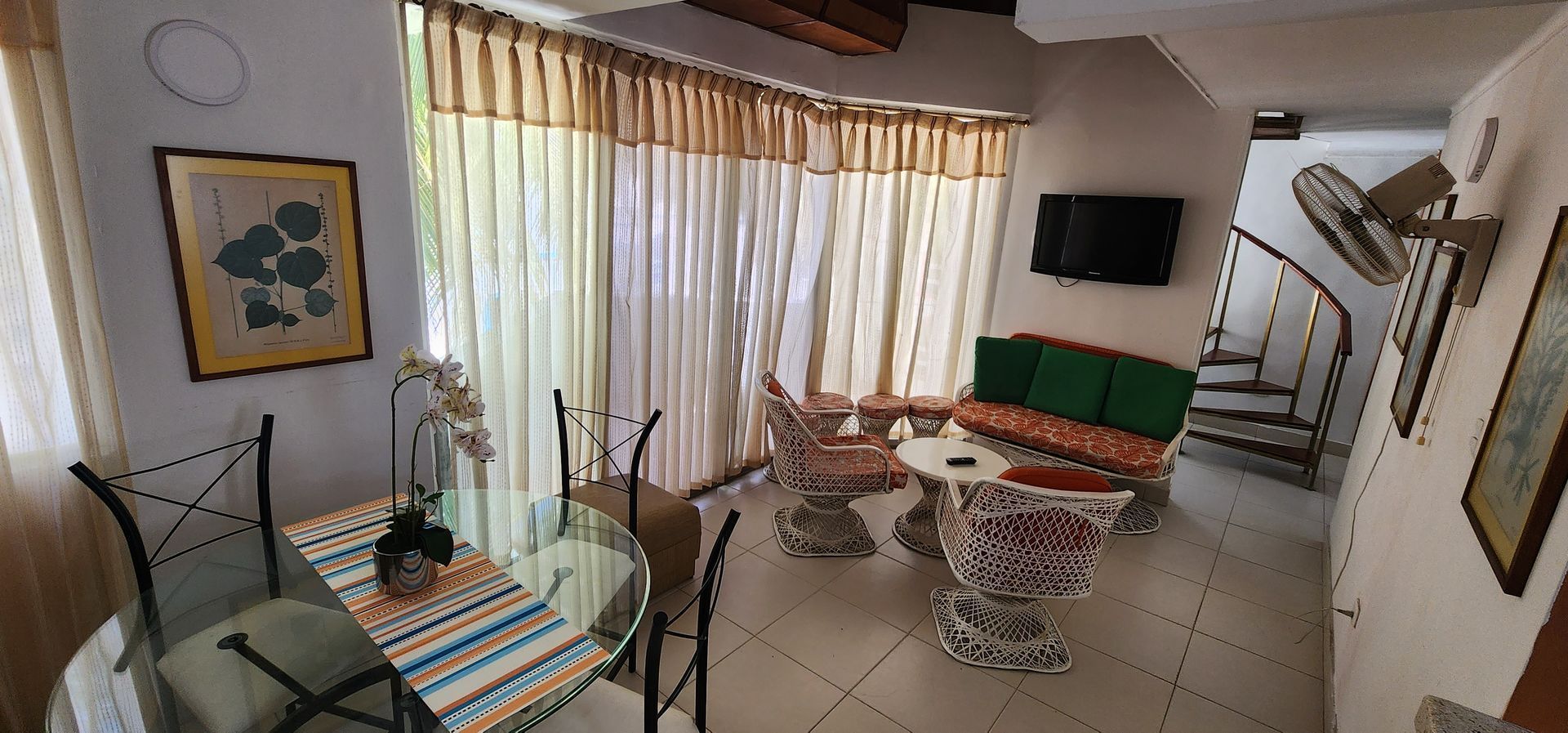 Una sala de estar y comedor con una mesa de cristal, sillas, un sofá con cojines verdes y una escalera de caracol.