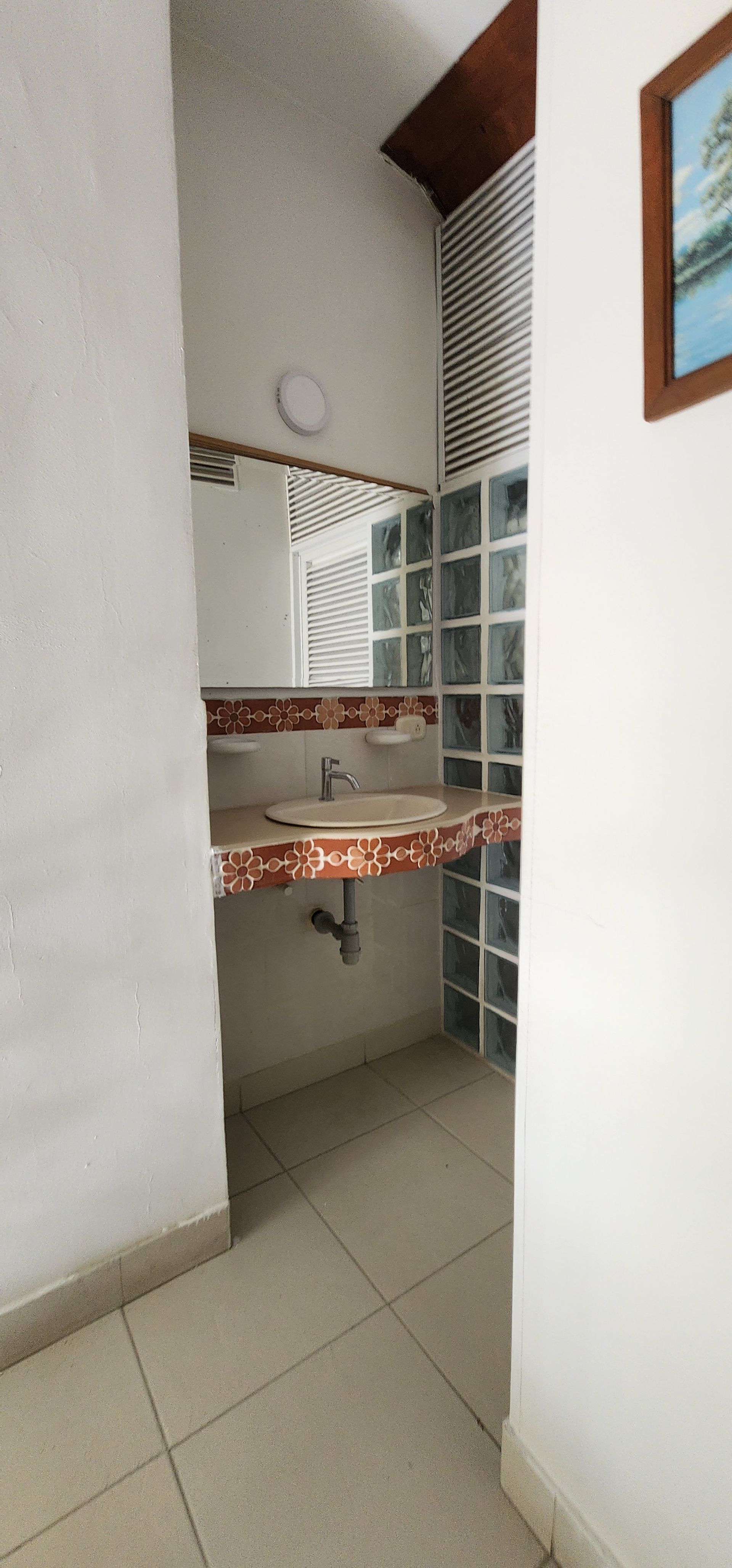 Un tocador de baño con encimera de piedra estampada y un espejo contra una pared de bloques de vidrio cuadrados.